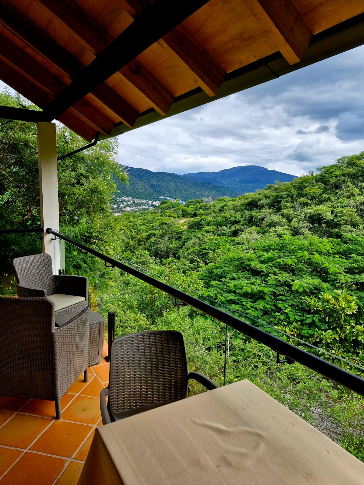 Terraza de la Cabaña Las Águilas con sillas de mimbre y vista a las montañas verdes.