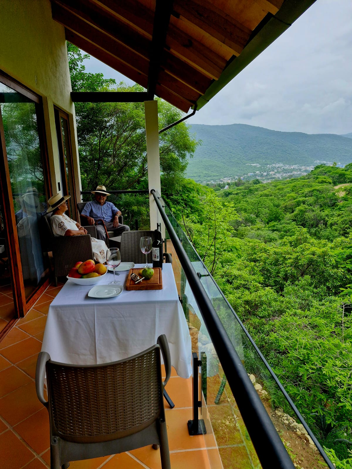 Terraza de la Cabaña Las Águilas con mesa servida, vino y frutas, y dos personas disfrutando de la vista.