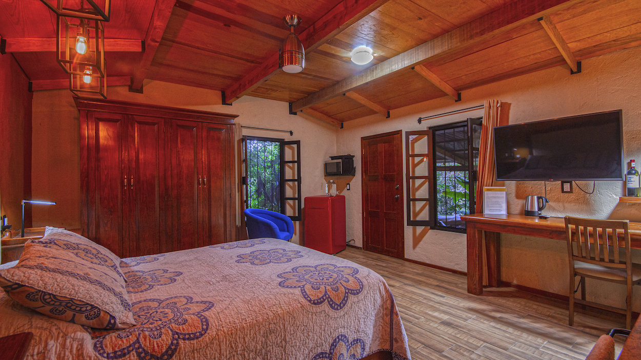 Interior de la Cabaña Mariposas con cama Queen, clóset, escritorio, televisor, refrigerador rojo y ventanas con vista al jardín
