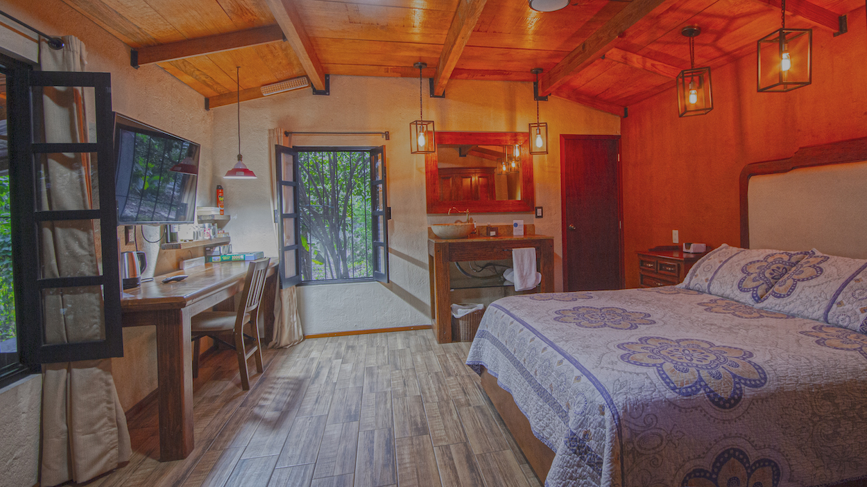 Habitación de la Cabaña Mariposas con cama Queen, escritorio con cafetera y TV, lavabo integrado y ventanas abiertas con vista al jardín