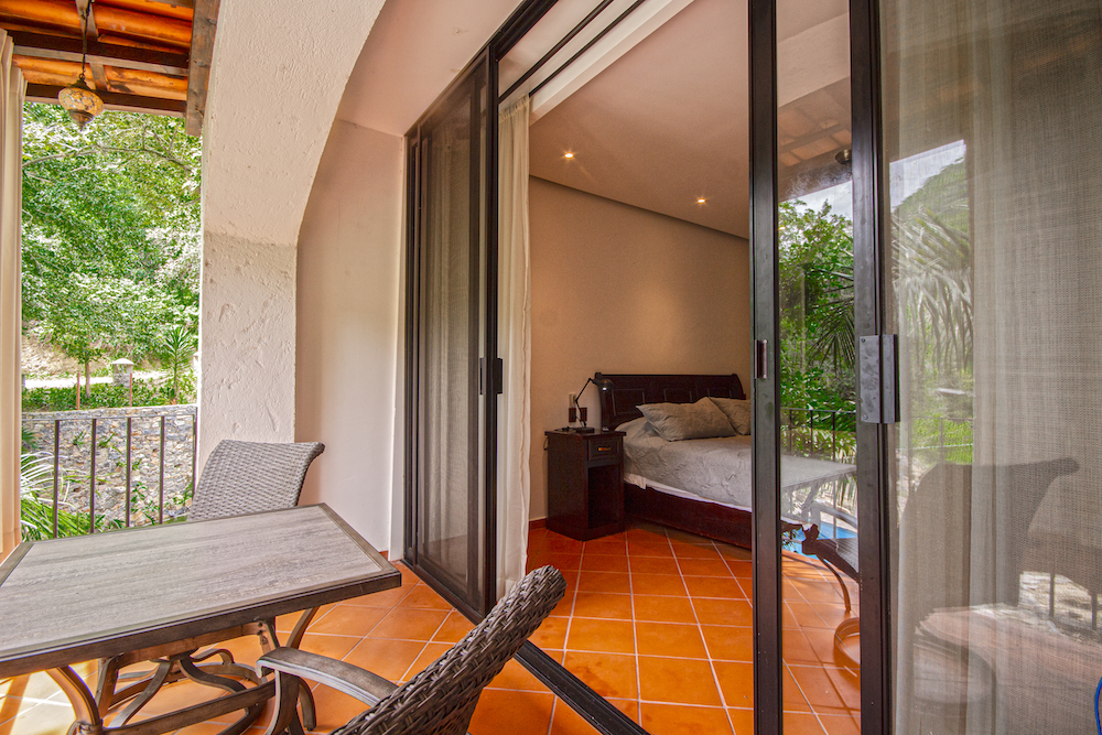 Terraza exterior de la Habitación El Cardenal con mesa y sillas de ratán y vista a la vegetación.