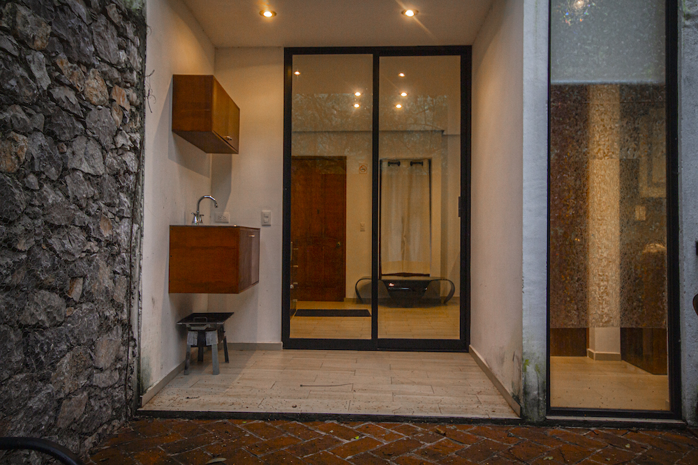 Entrada trasera de la Habitación El Jardín Secreto con ventanales, tarja y detalles en piedra junto a la vegetación.