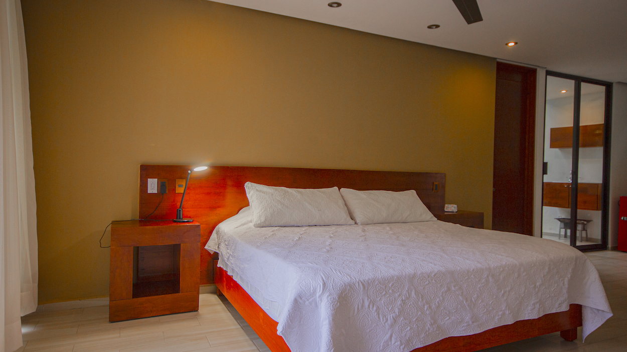 Detalle de la cama en la Habitación El Jardín Secreto con lámpara de noche y muros cálidos.