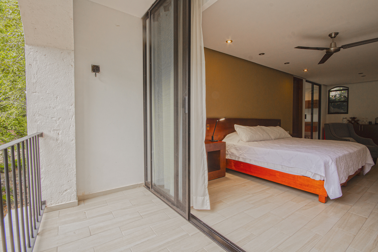 Balcón de la Habitación El Jardín Secreto con vista parcial a la recámara y barandal con vegetación al fondo.