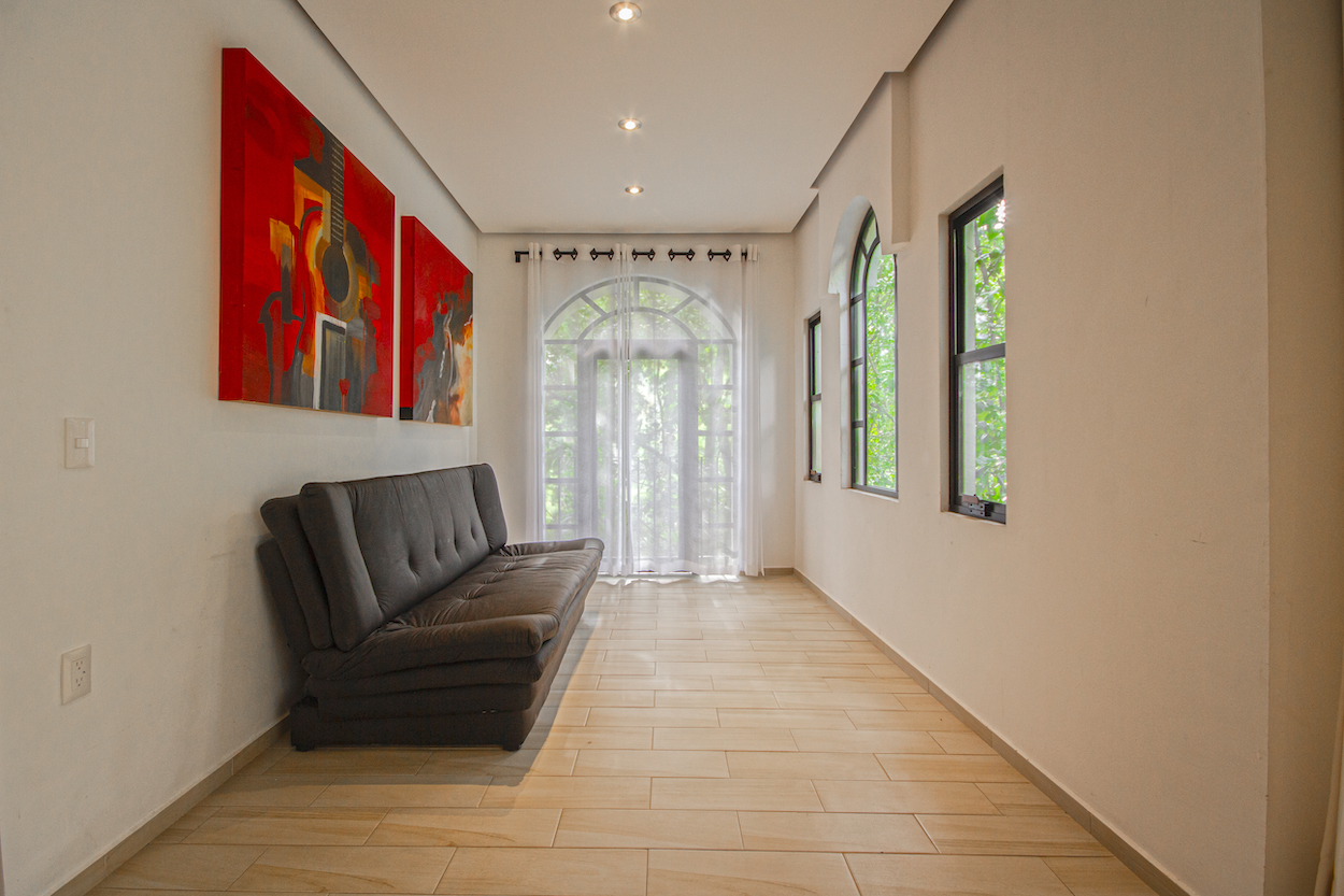 Sala interior de la Habitación El Jardín Secreto con sofá, cuadros rojos y grandes ventanales con cortinas blancas.