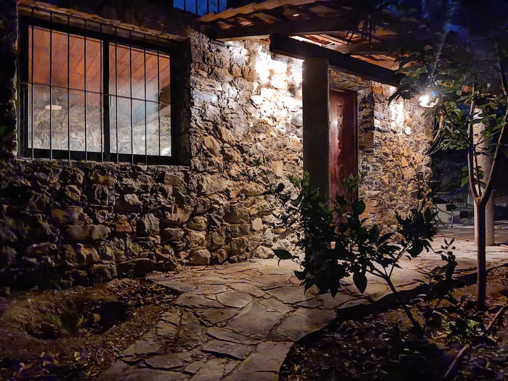Fachada nocturna de la Habitación San Francisco con muros de piedra, iluminación cálida y camino de laja rodeado de vegetación.