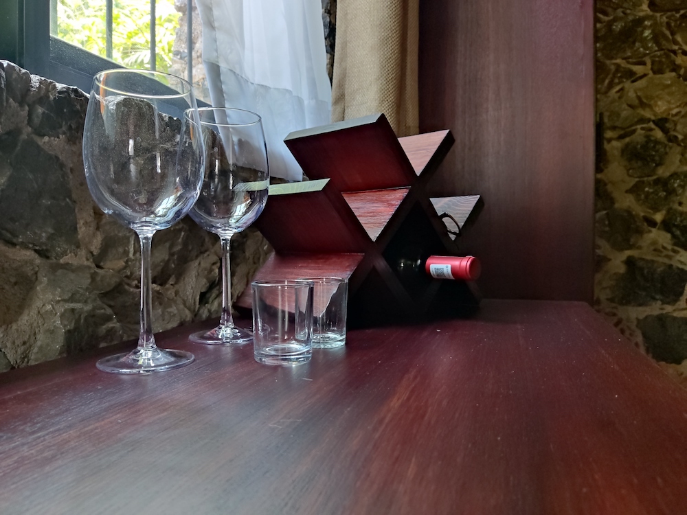 Detalle sobre el escritorio de la Habitación San Francisco con dos copas de vino, dos vasos, y un botellero con botella de vino junto a la ventana.