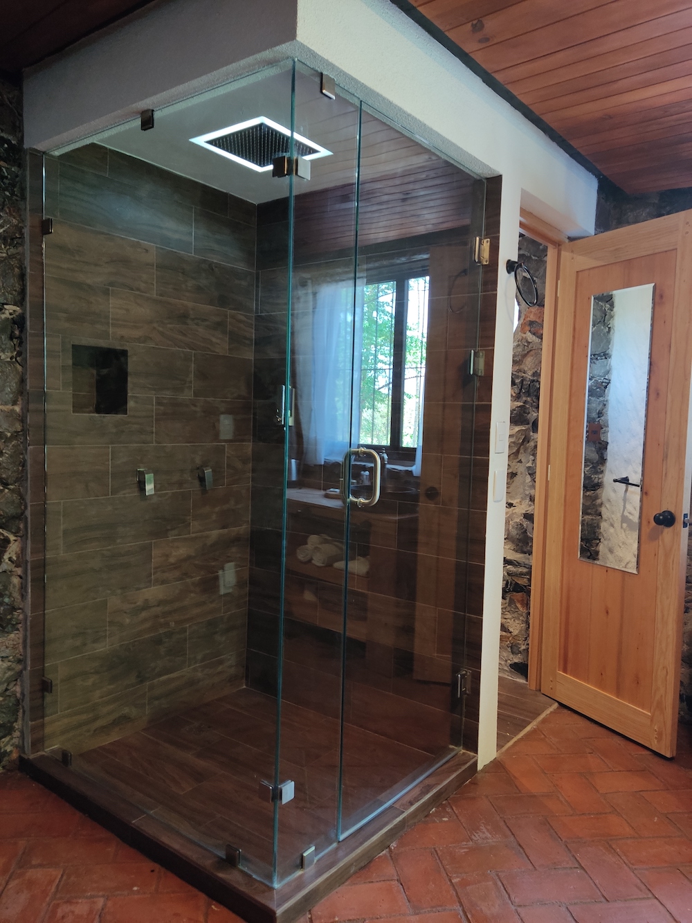 Baño de la Habitación San Francisco con regadera tipo lluvia dentro de una cabina de cristal y detalles en madera.