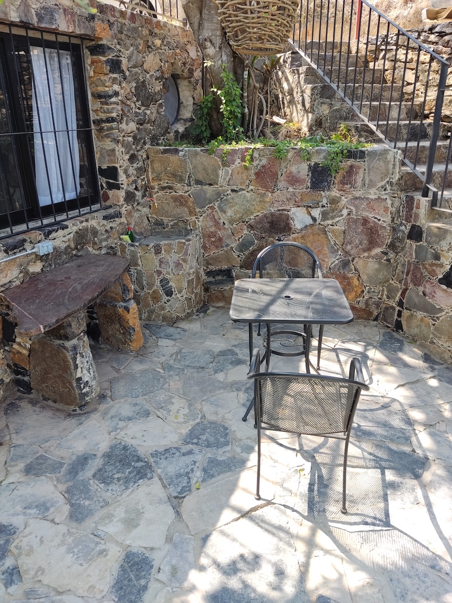 Terraza exterior de la Habitación San Francisco con mesa y dos sillas de metal sobre piso de piedra, junto a un muro rústico y vegetación.